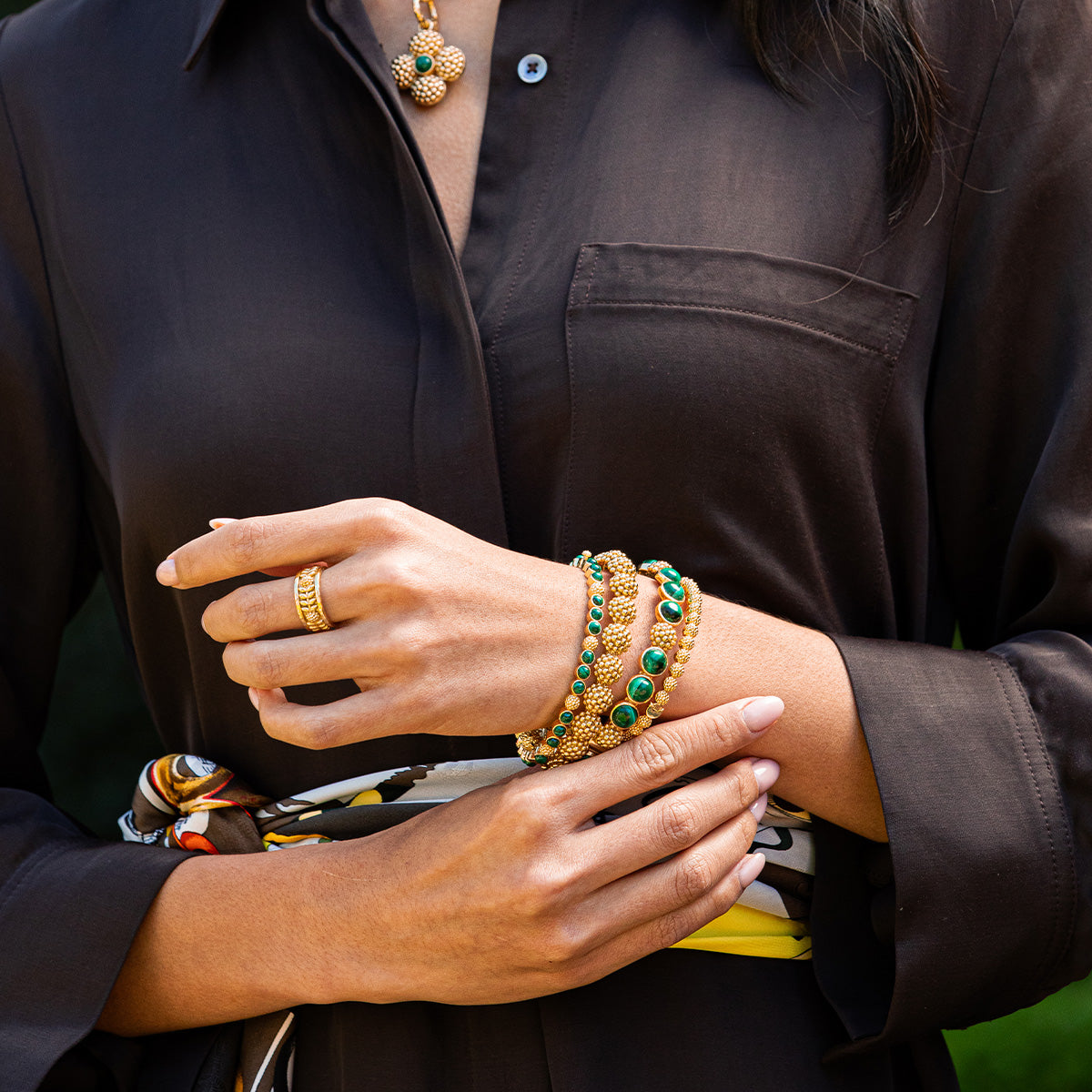 Close-up of a person wearing gold and green jewelry with a dark shirt.
