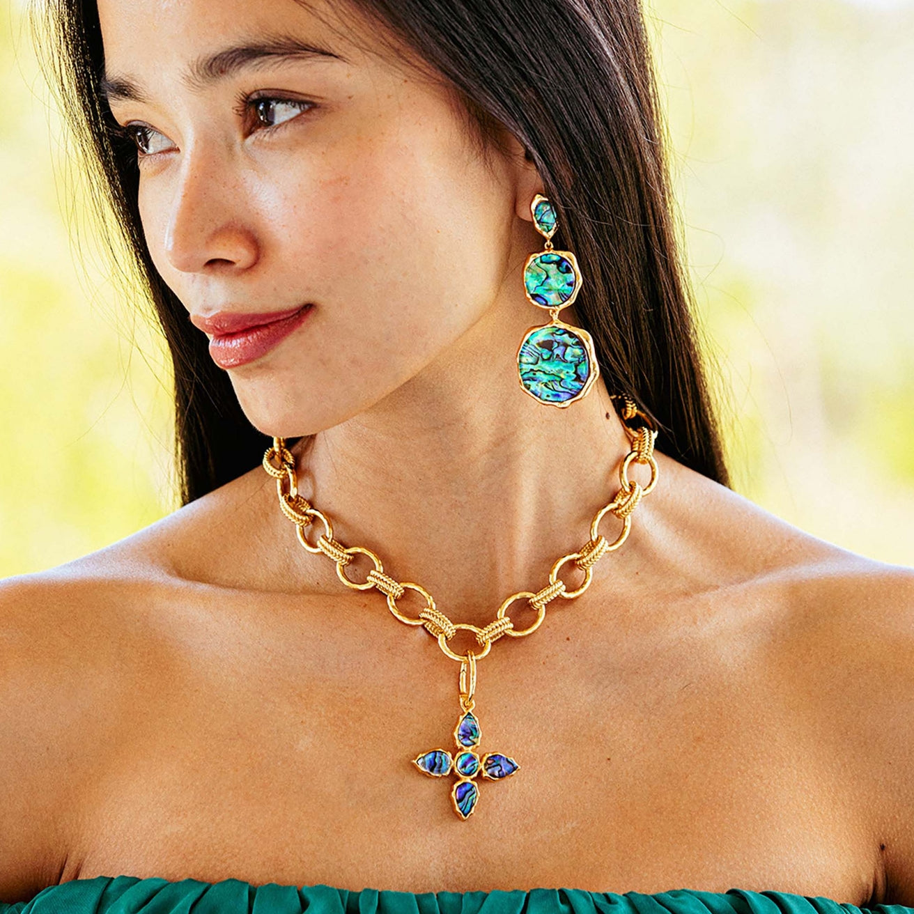 Woman wearing a gold chain necklace with a pendant and colorful earrings against a blurred background