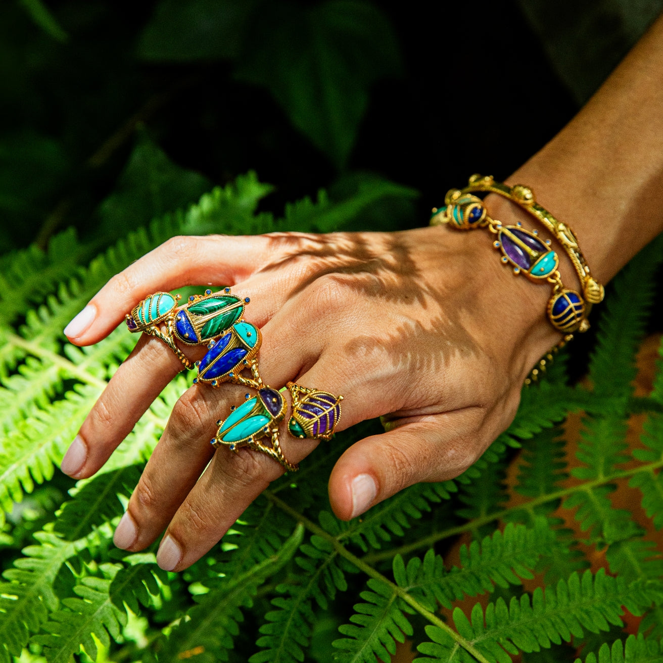 Hand wearing multiple gold rings with gemstones on a leafy background