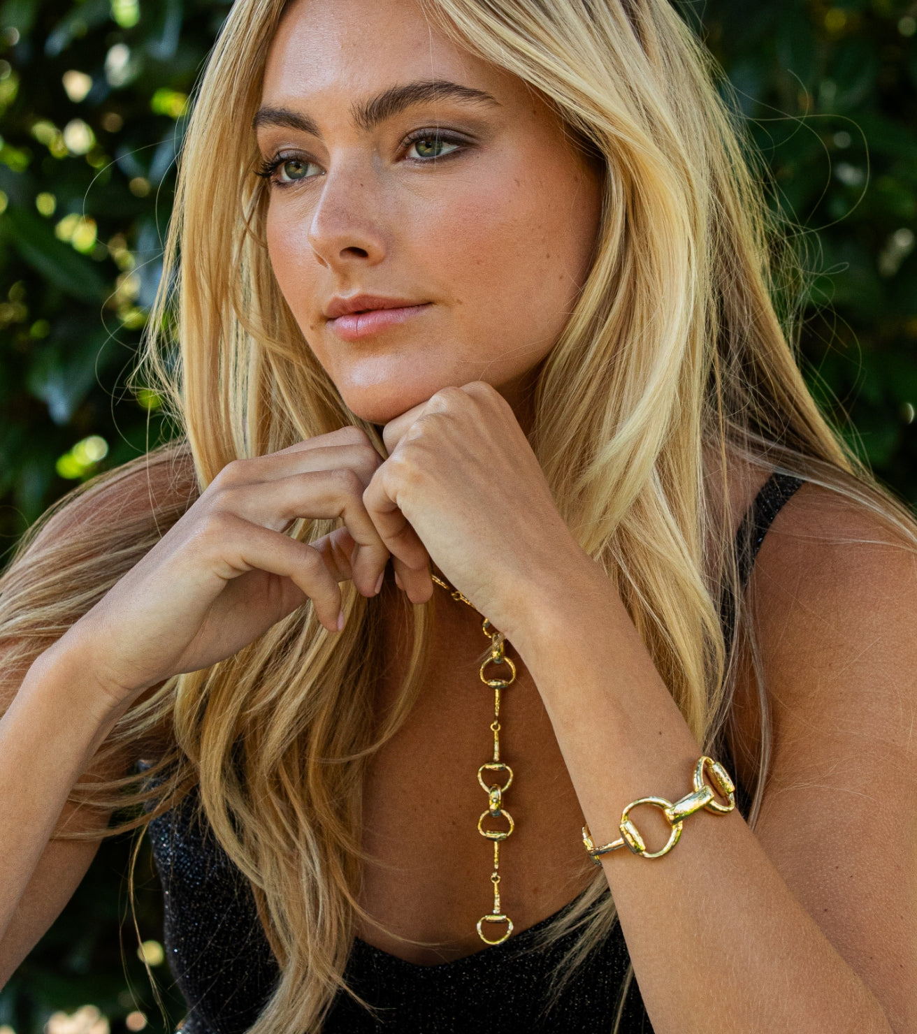 Woman wearing gold jewelry with a blurred green background