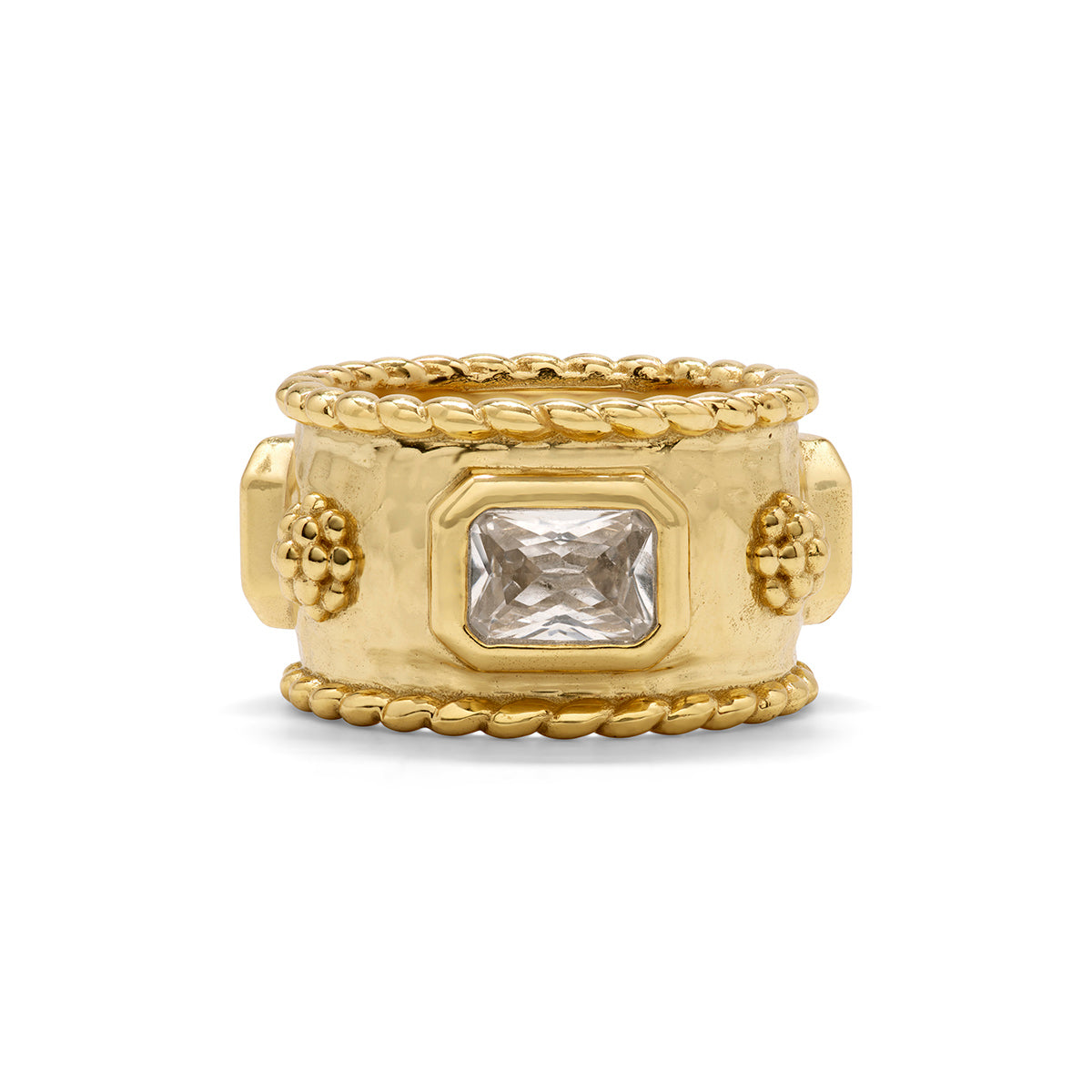 A wide yellow gold ring with a textured hammered center, a rectangular clear gemstone, and decorative grape motifs on the sides, framed by rope-textured borders on a white background.