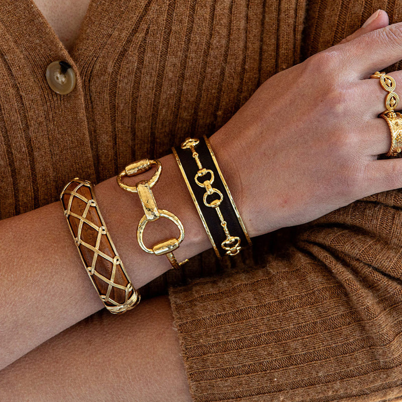 Three bracelets in gold, teak and forest pop against a light brown sweater.