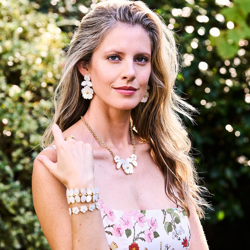 Woman looking into camera smiling wearing floral mother-of-pearl jewelry. 
