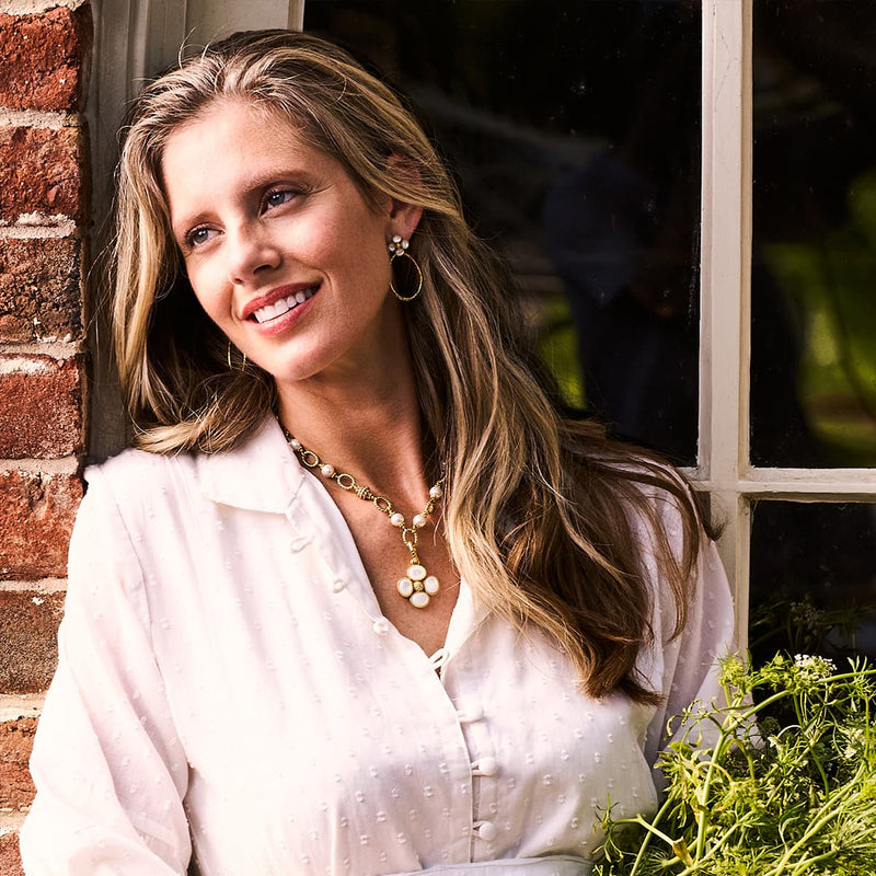 A woman smiling and looking off into the distance with gold earrings and a gold necklace