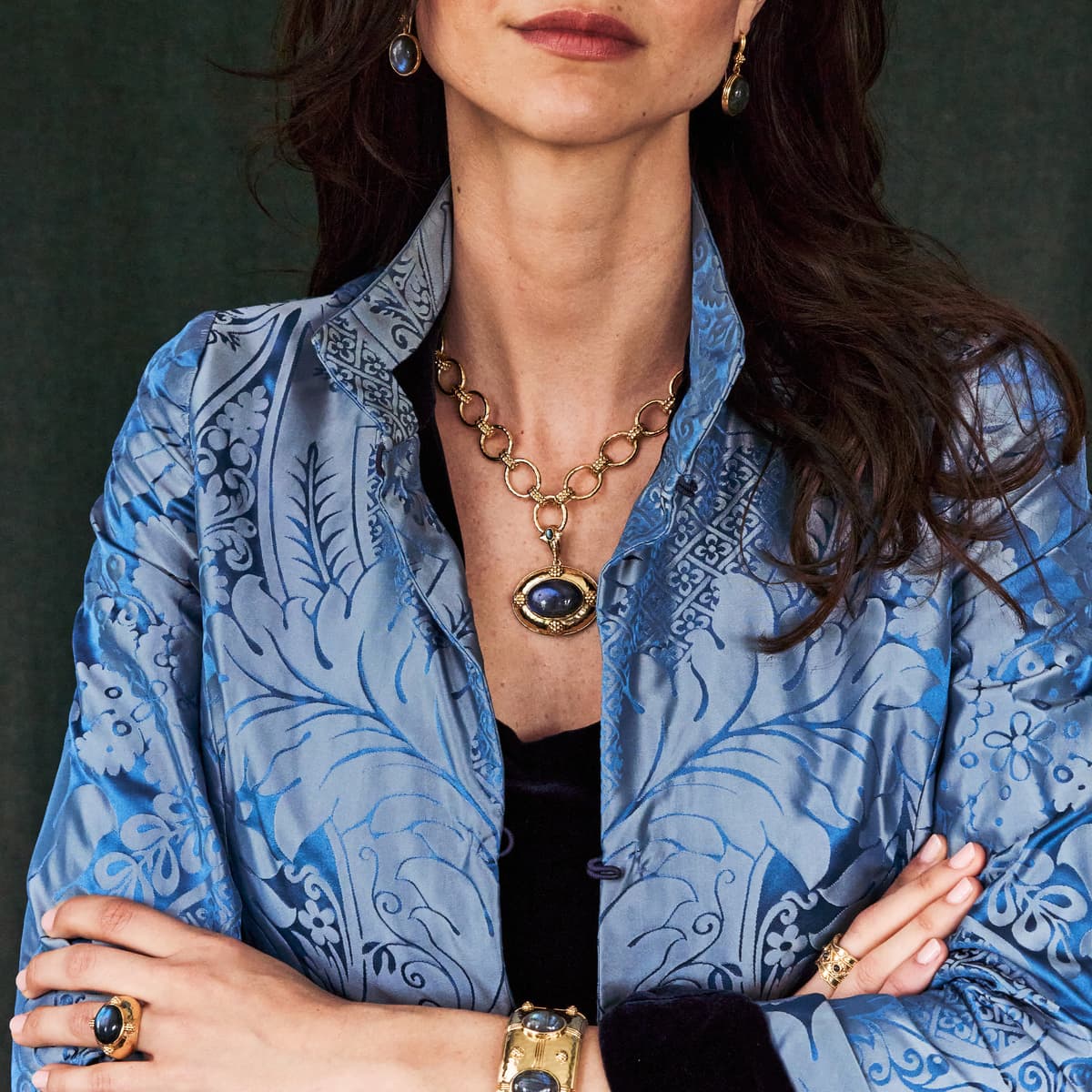 Woman wearing a blue patterned jacket with gold jewelry against a dark background