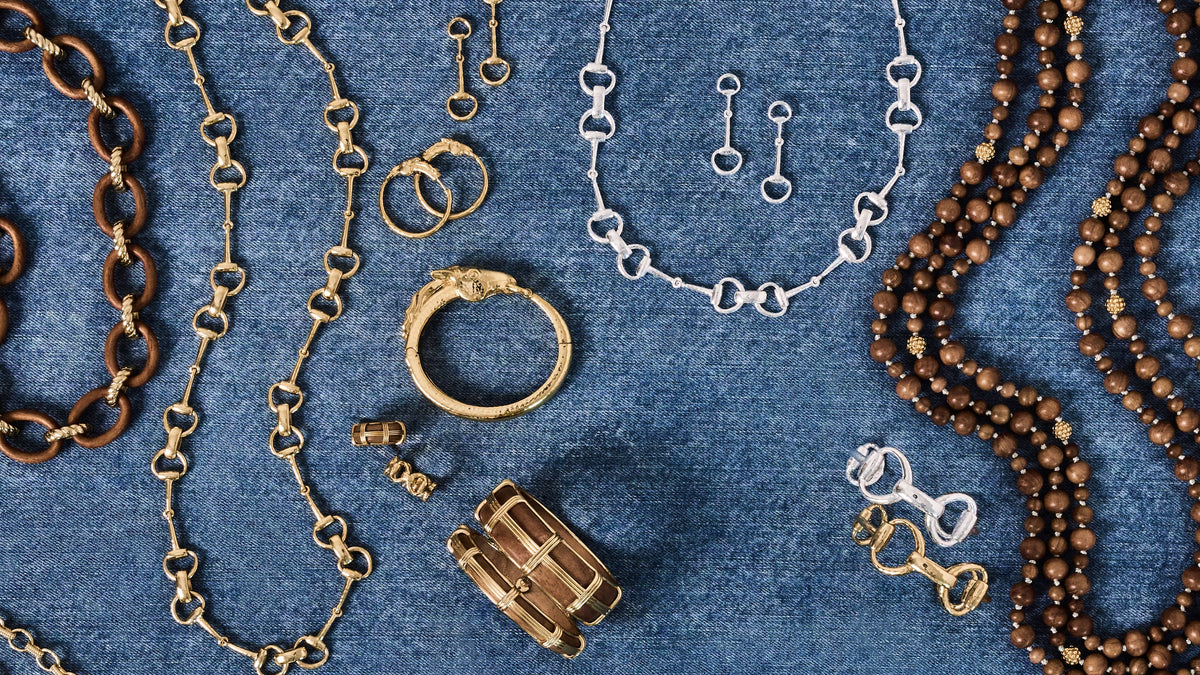 An assortment of jewelry pieces including gold and silver chains, rings, earrings, and beaded necklaces arranged on a textured blue denim background.
