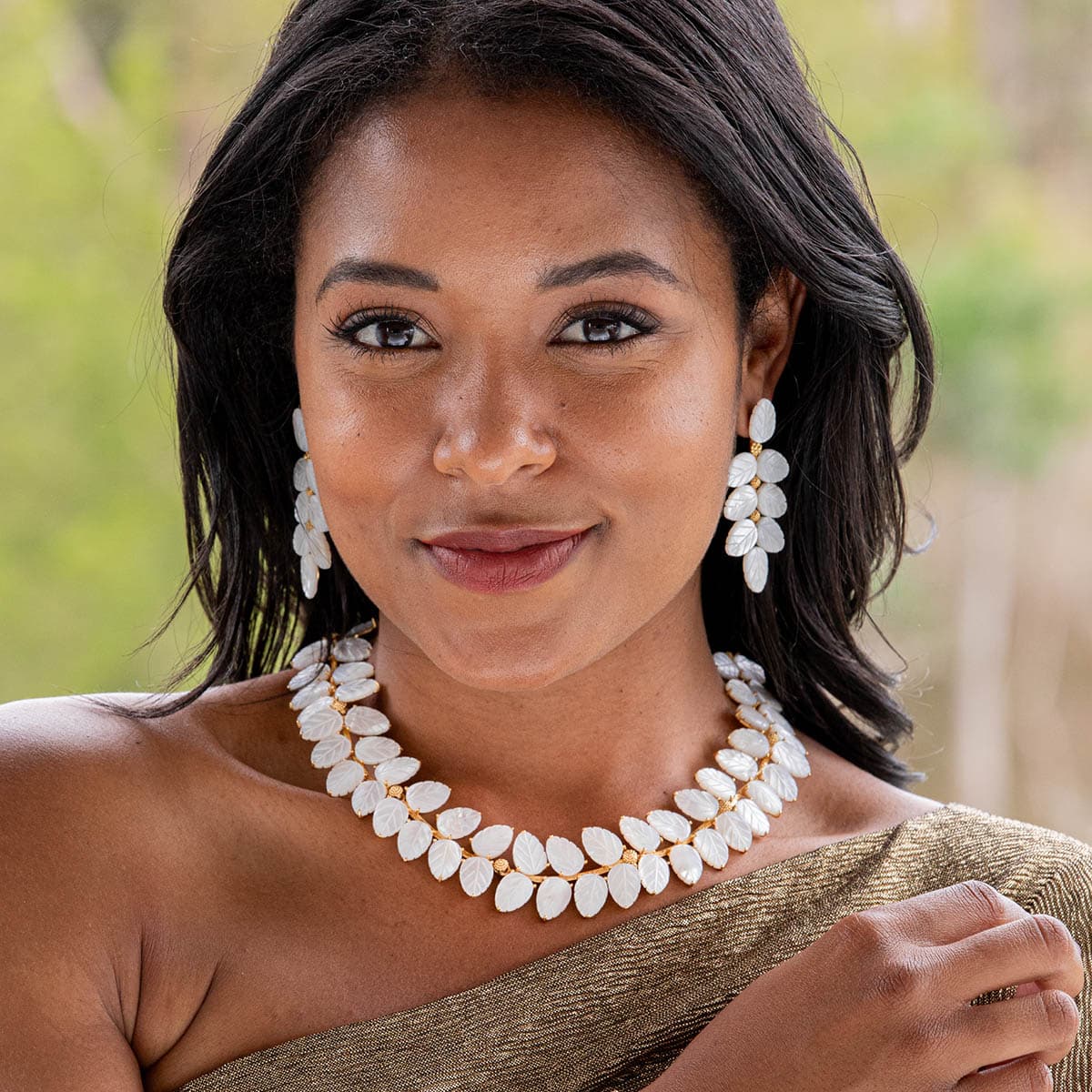 Woman wearing a white necklace and earrings with a blurred natural background