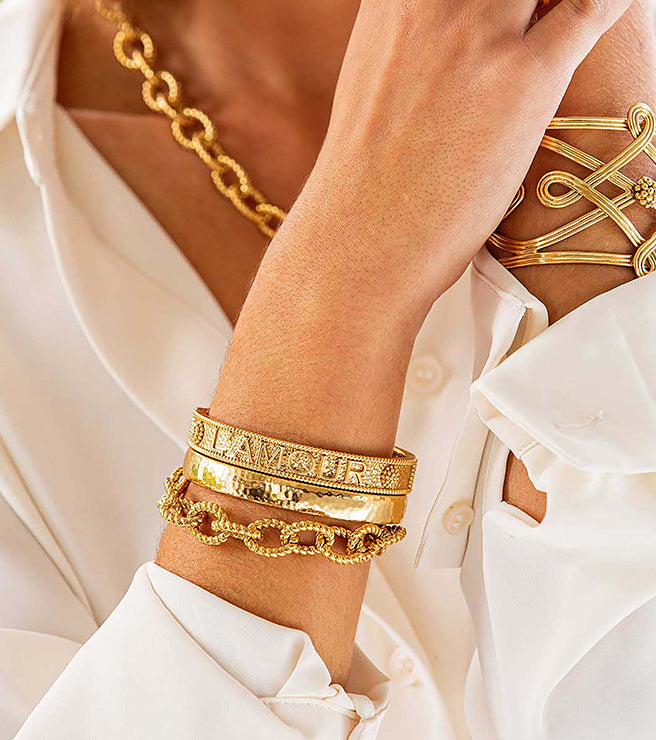 Gold jewelry including bracelets and a necklace on a person wearing a white shirt.