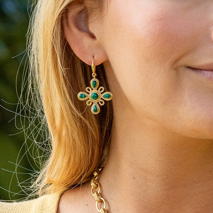 Close-up of a person wearing gold earrings with green gemstones.