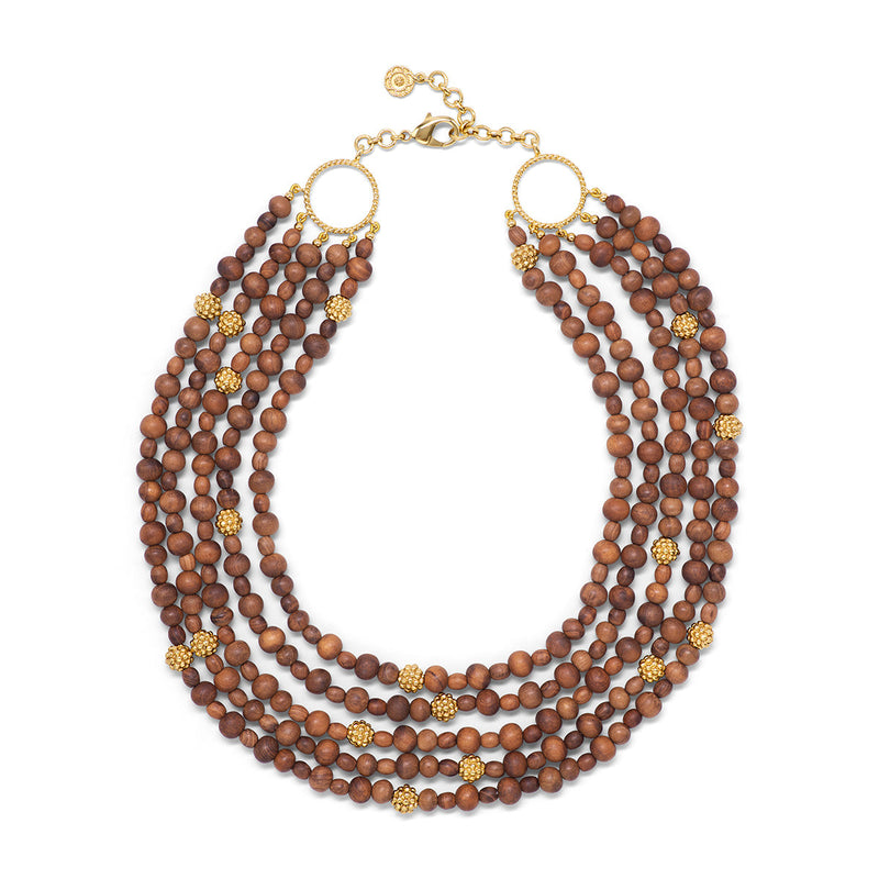 Our twist on classic statement pearls, this subtly striking necklace is composed of five strands of lustrous teak beads that are hand-carved into decadent little orbs and embellished with exquisite details like a sprinkling of golden berries. Inspired by Mother Nature who is a masterclass in slow beauty and how to make an impact in an understated way — or a grand entrance when she wants to.