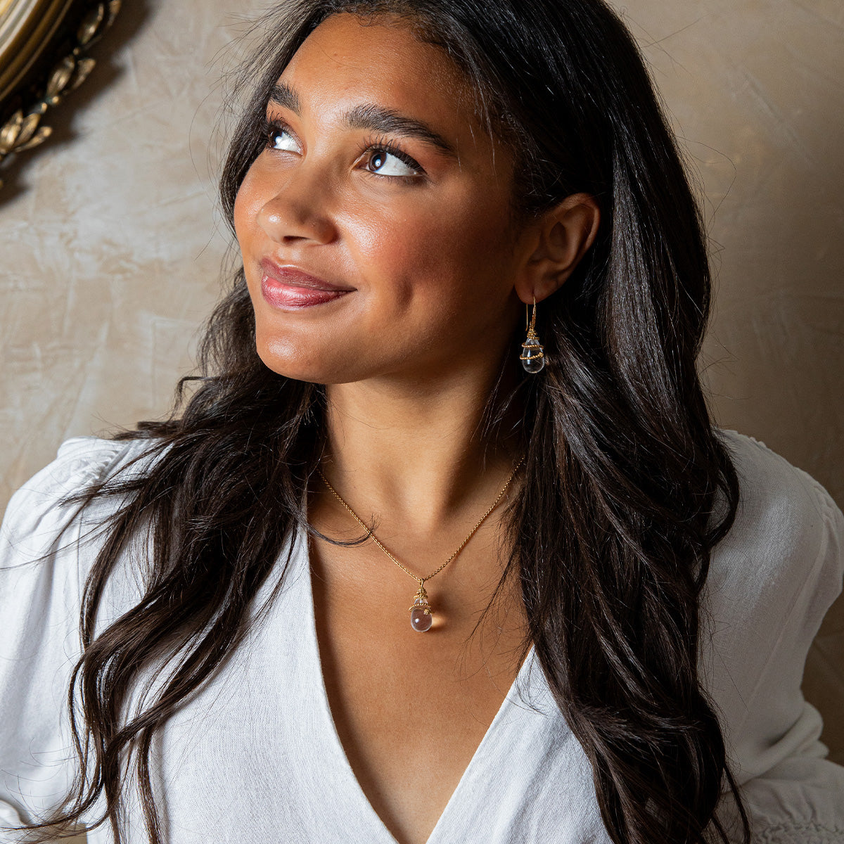 Woman wearing a necklace and earrings against a neutral background