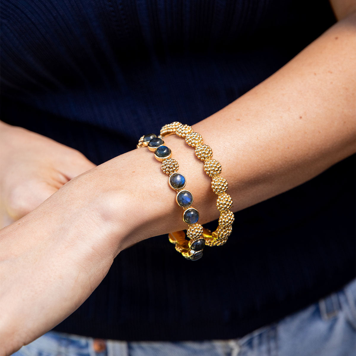 Gold bracelet with blue stones on a person's wrist against a dark background