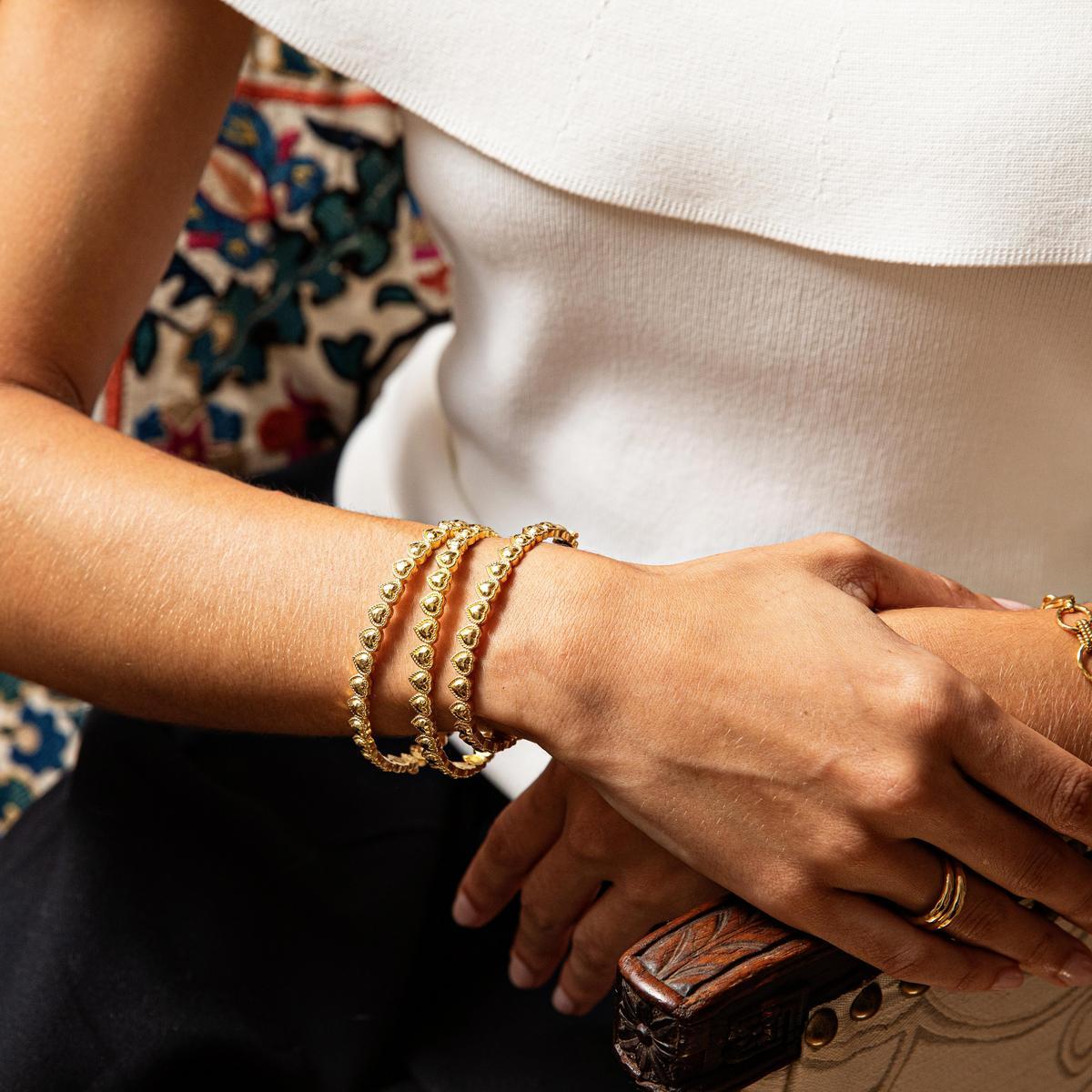 Close-up of a person's wrist wearing gold love petite bracelets