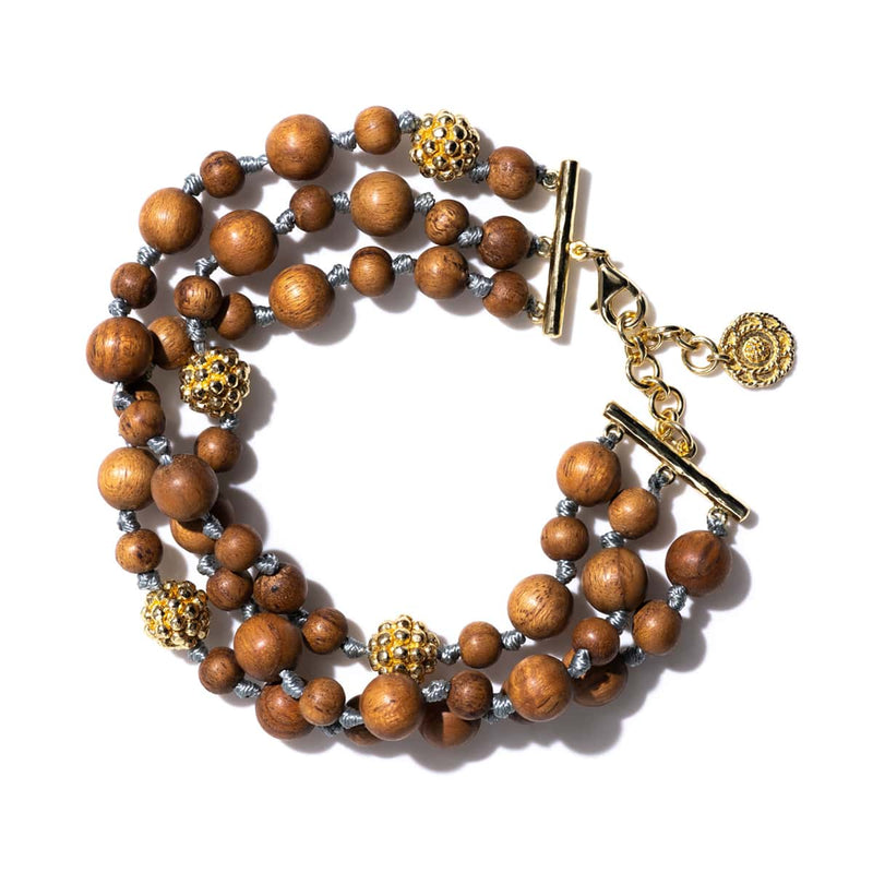 Hand-carved teak wood beads are strung and knotted like pearls and sprinkled with little golden berries for an effect that is simultaneously exotic and understated. Exuding the warmth of Mother Nature, the lustrous little orbs click and clack to their own rhythm throughout the day, a reminder to always move to the beat of your own drum and stay grounded. And they are really fun to fiddle with while daydreaming or hatching a brilliant plan.